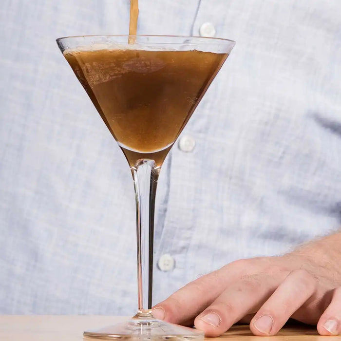Espresso Martini steht auf einem Tisch mit einer Hand im Hintergrund  