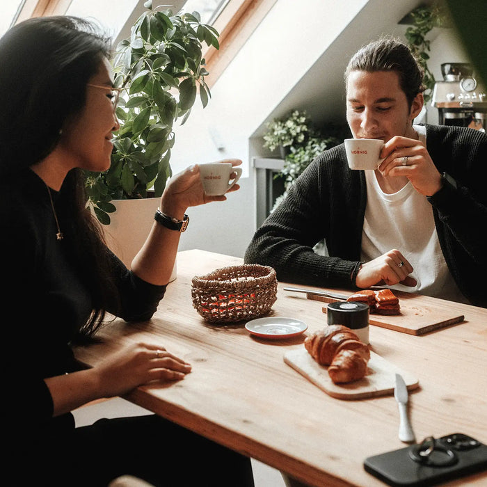 Zwei Personen sitzen in einer Büroküche und trinken Kaffee.