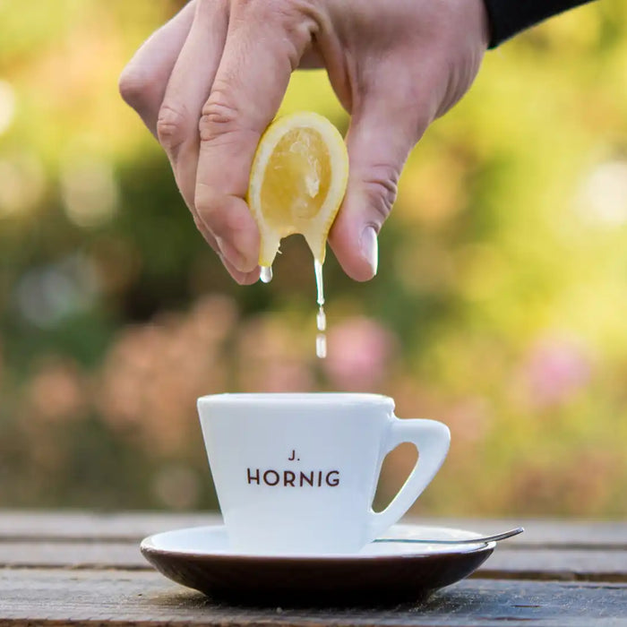 Eine Hand zerdrückt eine Zitrone über einer J. Hornig Espressotasse mit Untertasse 