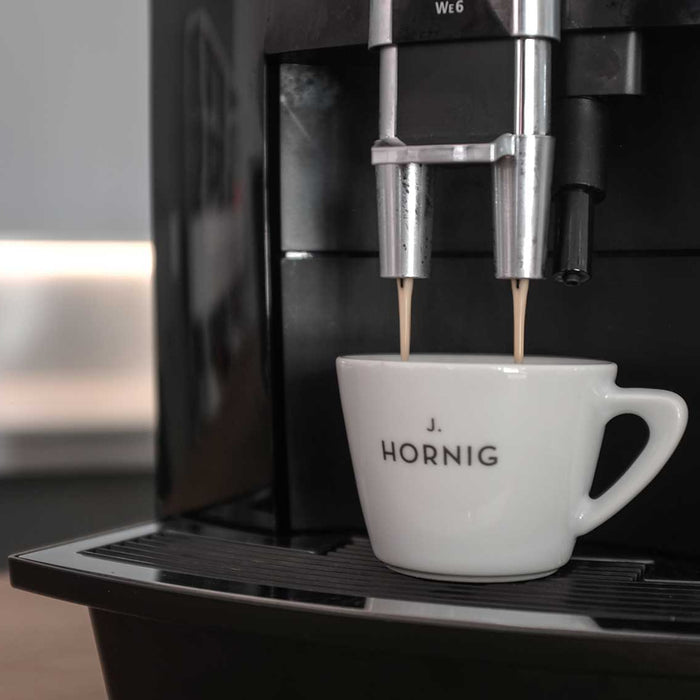 Kaffee rinnt von einem Kaffeevollautomaten in eine weiße J. Hornig Tasse 