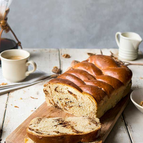 Das vegane Walnuss-Kaffee-Osterbrot liegt auf einem Brett aufgeschnitten, daneben steht eine Schüssel mit zerhackten Walnüssen und ein Becher Kaffee