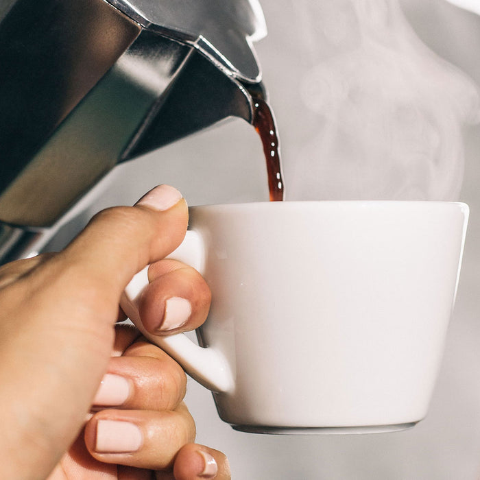 Aus einer Bialetti in eine weiße Tasse wird Kaffee eingeschenkt 