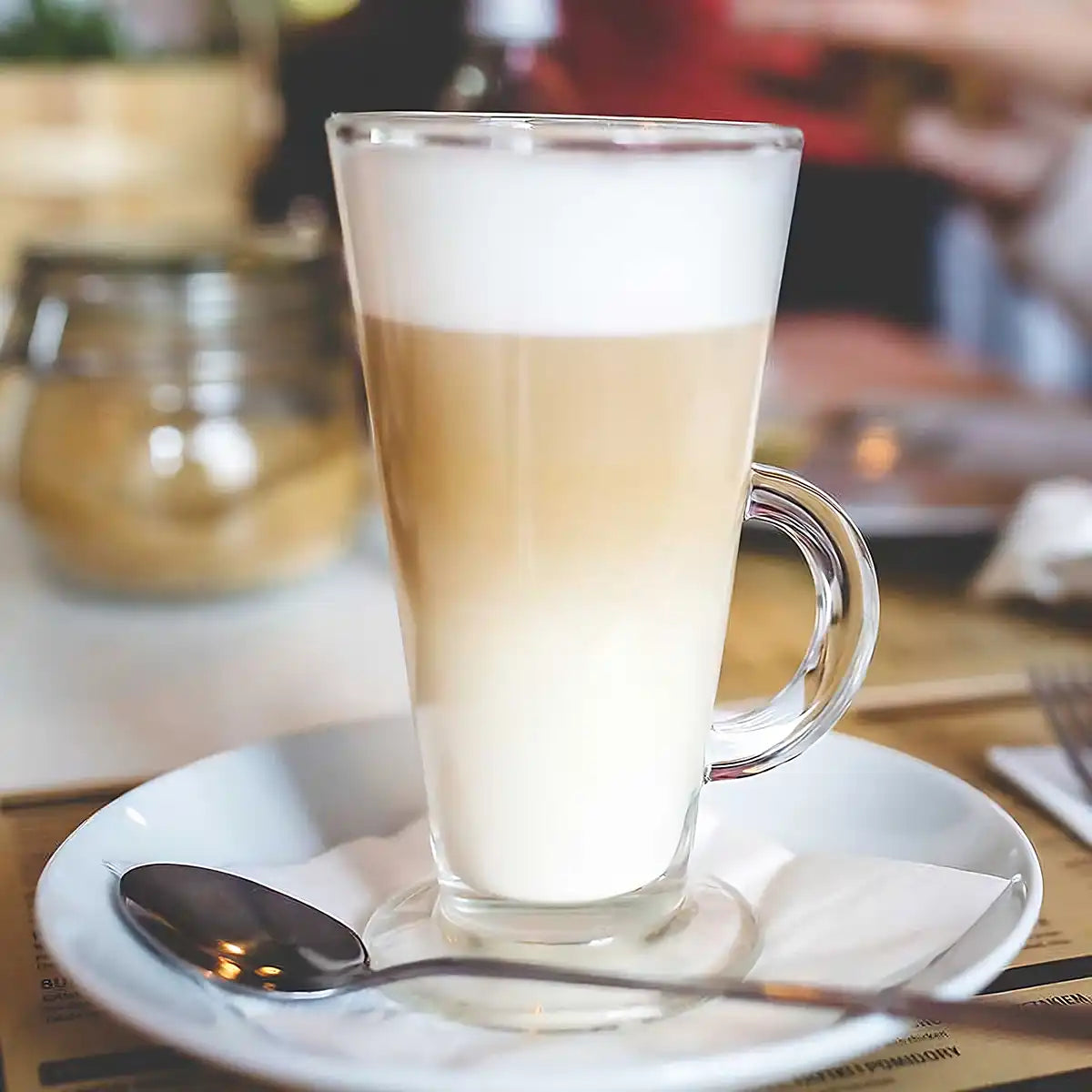 Ein Latte Macchiato steht mit Untertasse und Löffel auf einem Tisch 