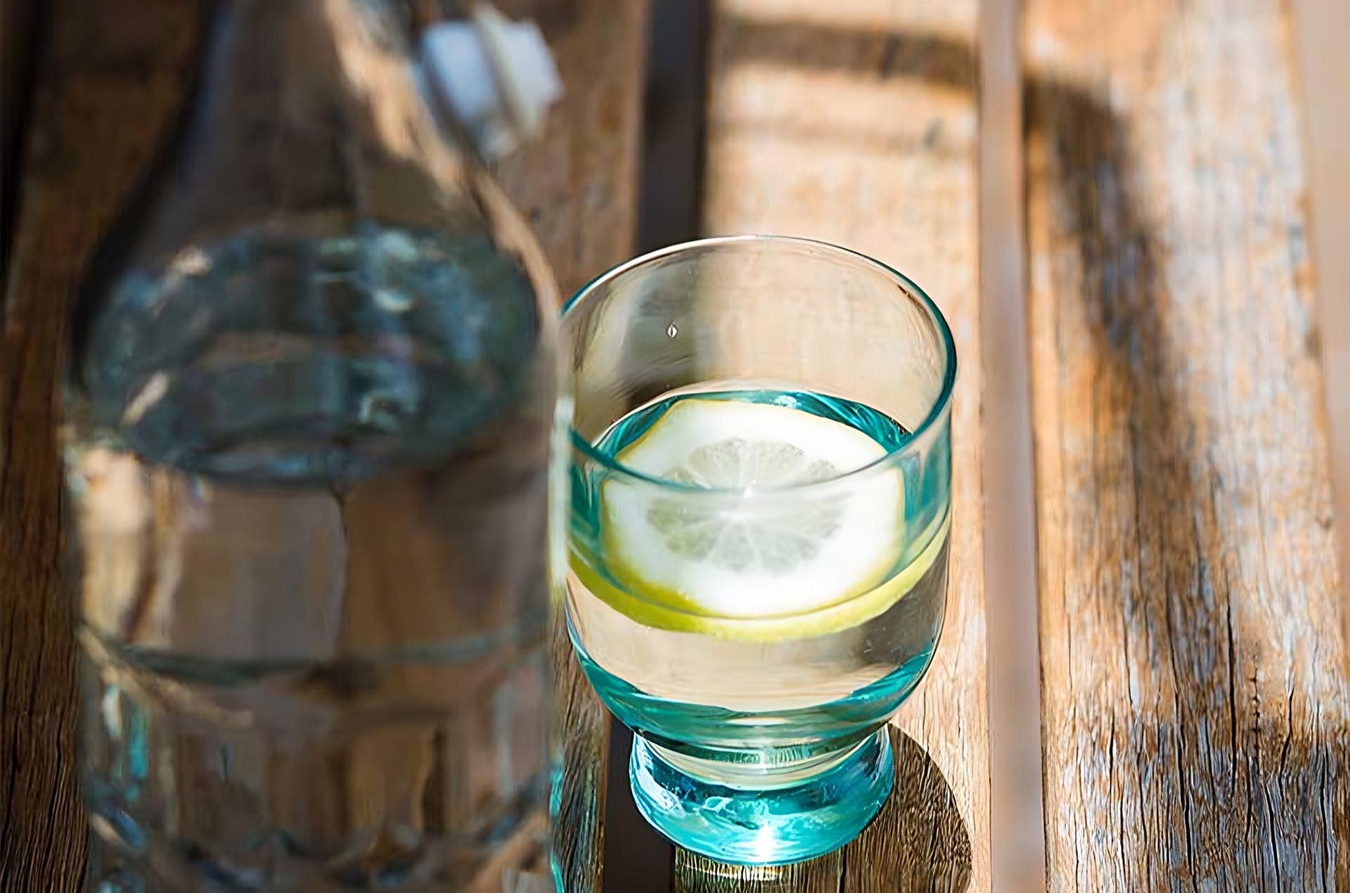 Eine Flasche Wasser und ein Glas Wasser mit Zitrone stehen auf einer Holzbank