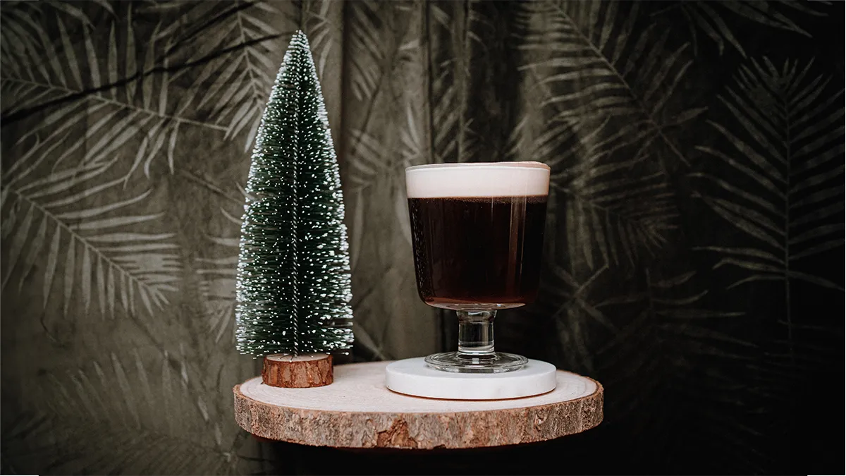 Ein Irish Coffee in einem Glas auf einem Holztablett auf dunklem Hintergrund.
