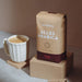 Eine Packung J. Hornig Alles Arabica Kaffee mit einer Cappuccinotasse auf hellem Untergrund und braunem Hintergrund