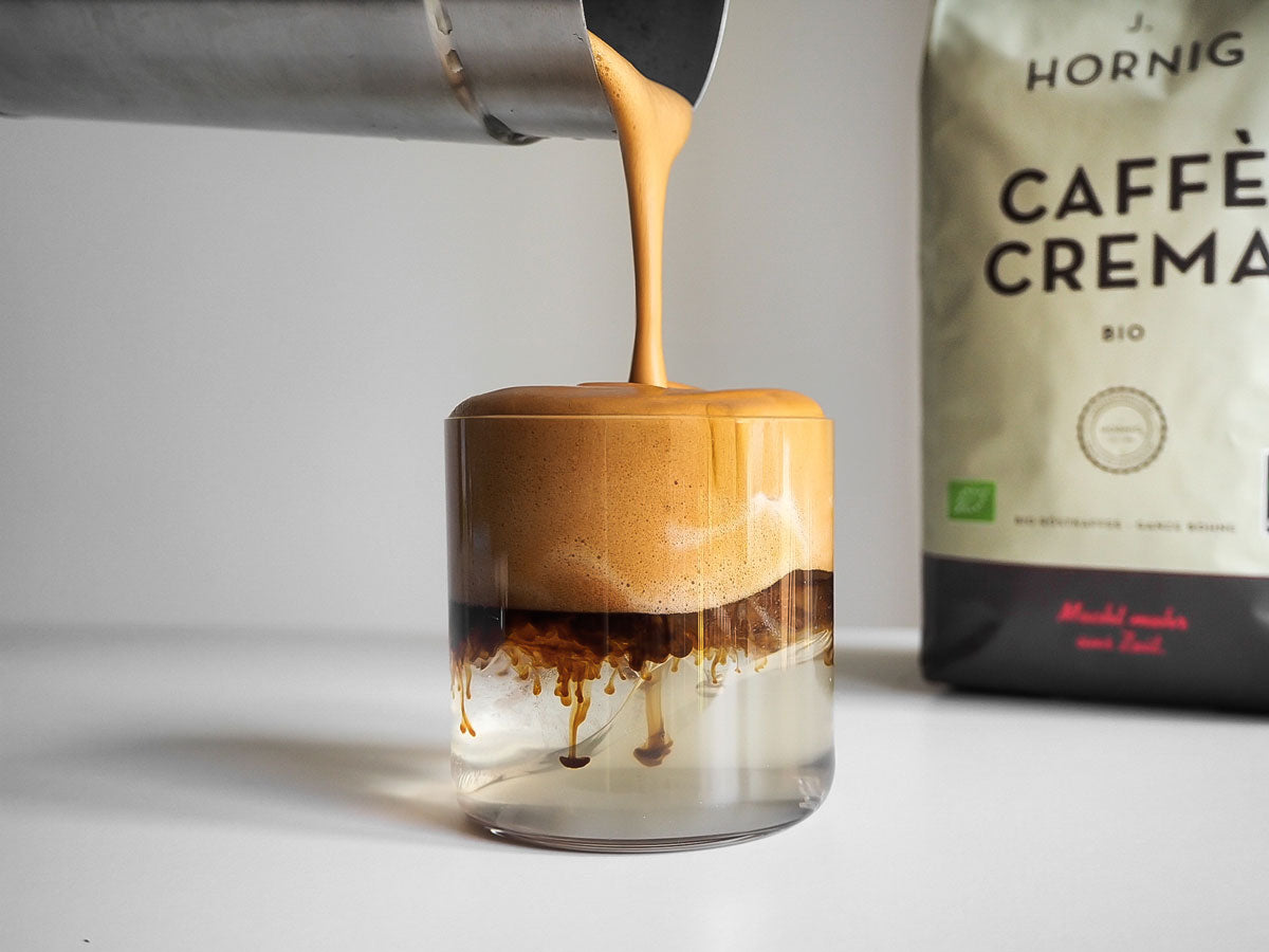 Eine Packung J. Hornig Caffè Crema Bio steht im Hintergrund, davor wird ein Cloud Coffee zubereitet.