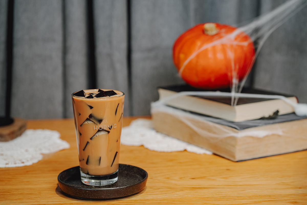 Ein Halloween Drink in einem J. Hornig Glas steht auf einem Holztisch, dahinter eine Halloween Dekoration mit Kürbis.