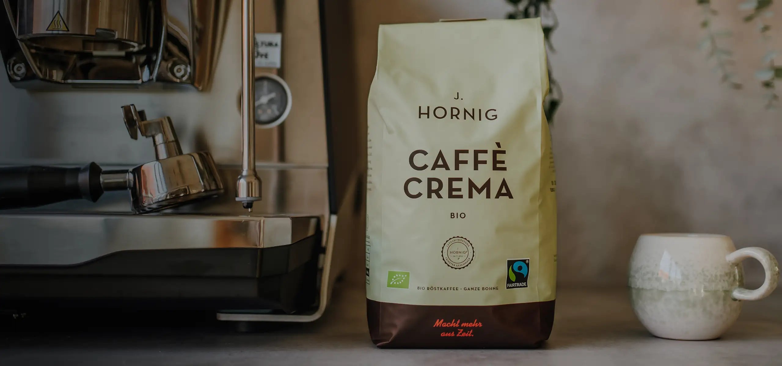 Eine Packung J. Hornig Caffe Crema Bio neben einer Siebträgermaschine und einer Kaffeetasse