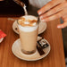 Ein Caffe Latte auf einem Holztisch mit einer J. Hornig Zucker-Packung.
