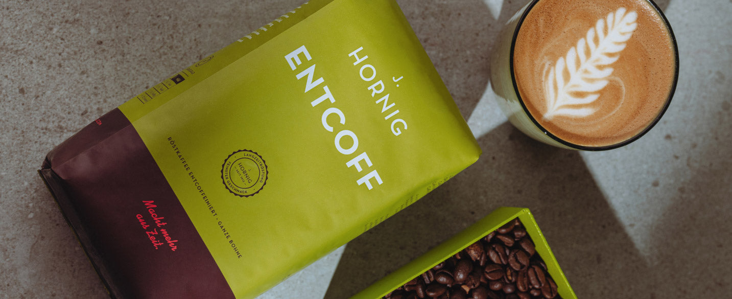 Eine Packung J. Hornig Entcoff liegt auf einer Tisch Platte daneben steht ein Cappuccino mit Latte Art