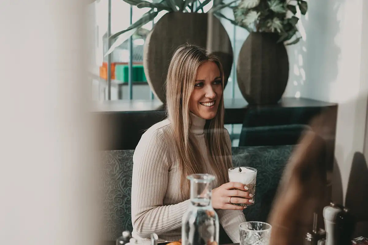 Eine junge Frau sitzt im Kaffeehaus und hält einen Kaffee in der Hand