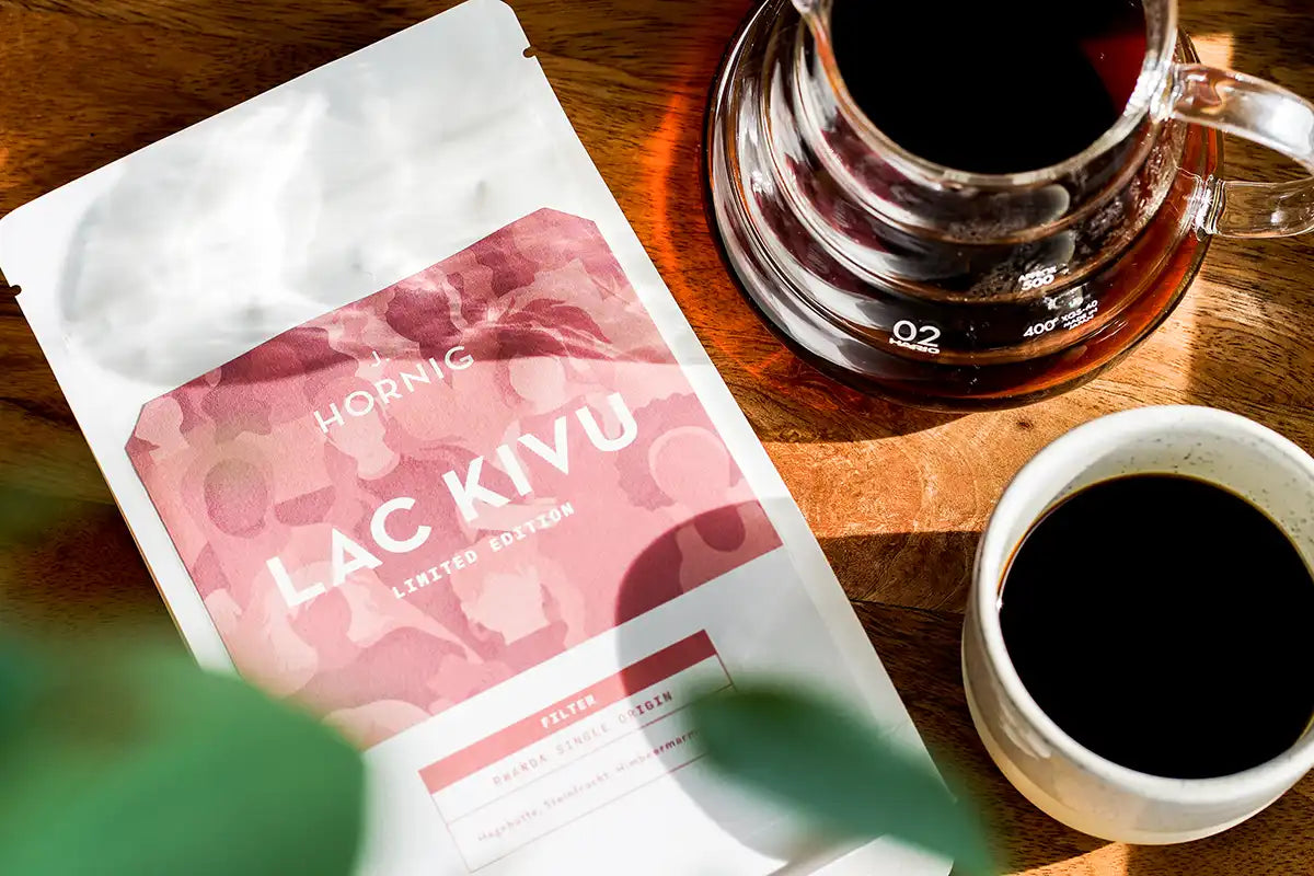 Eine Packung J. Hornig Spezialitätenkaffee Lac Kivu Filter auf einem Holz-Untergrund mit einer Tasse Kaffee