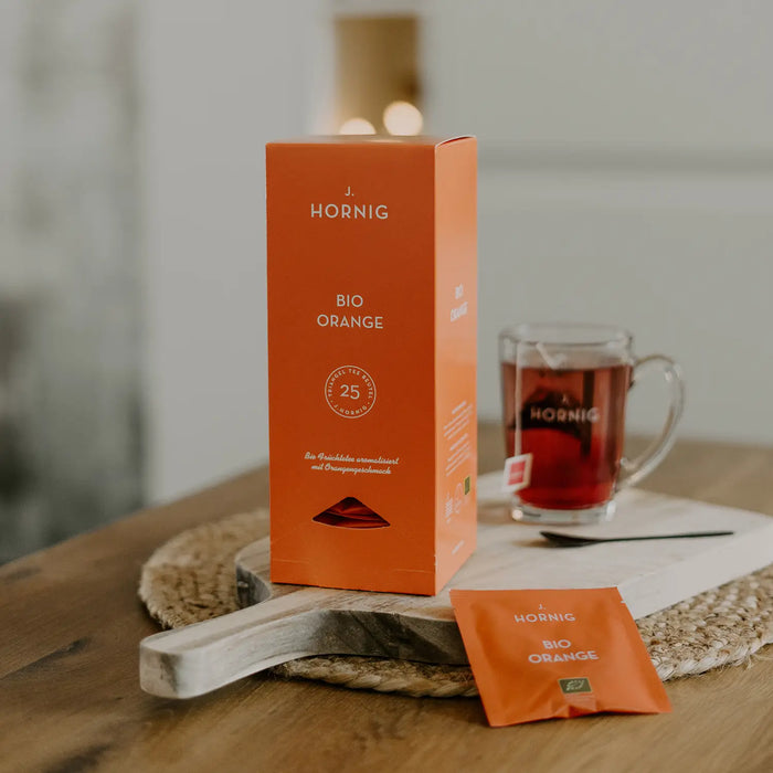 Eine Packung J.Hornig Bio Pyramidenbeutel Orange Tee auf einem Holztisch mit einer Tasse Tee.
