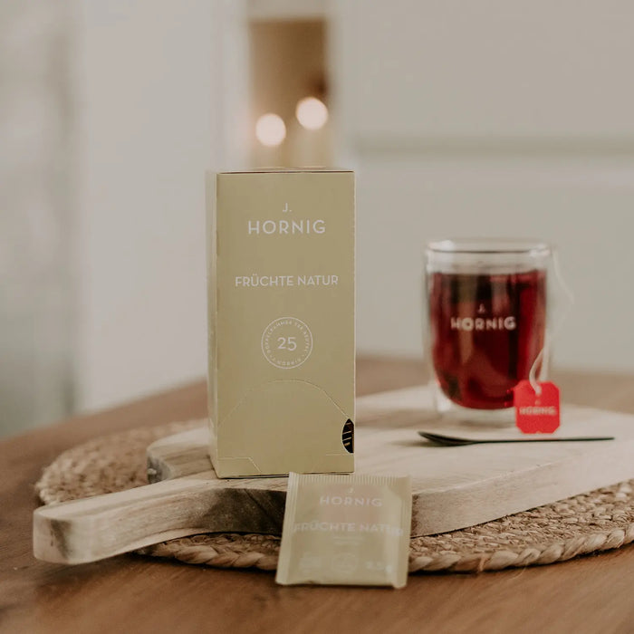 Eine Packung J.Hornig Doppelkammerbeutel Früchte Natur Tee auf einem Holztisch mit einer Tasse Tee