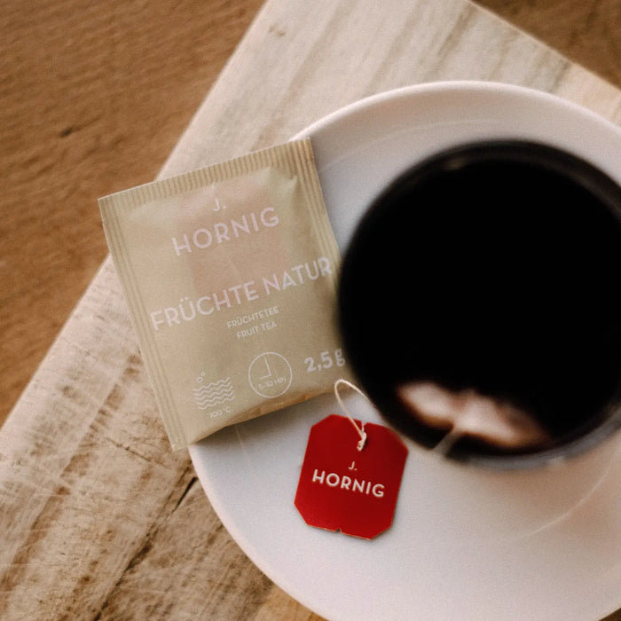 Eine Tasse Tee in einem J.Hornig Teeglas mit einer Einzelpackung Früchte Natur Tee..