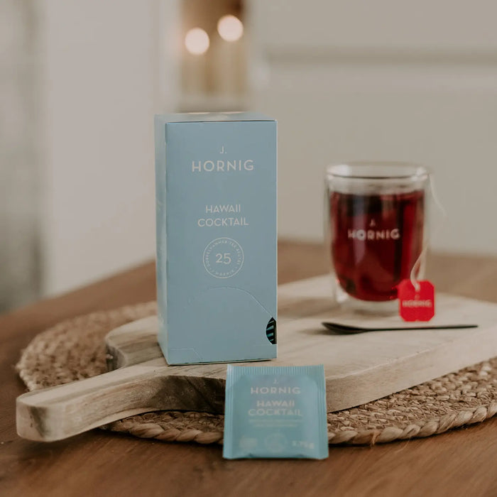 Eine Packung J.Hornig Doppelkammerbeutel Hawaii Tee auf einem Holztisch mit einer Tasse Tee.