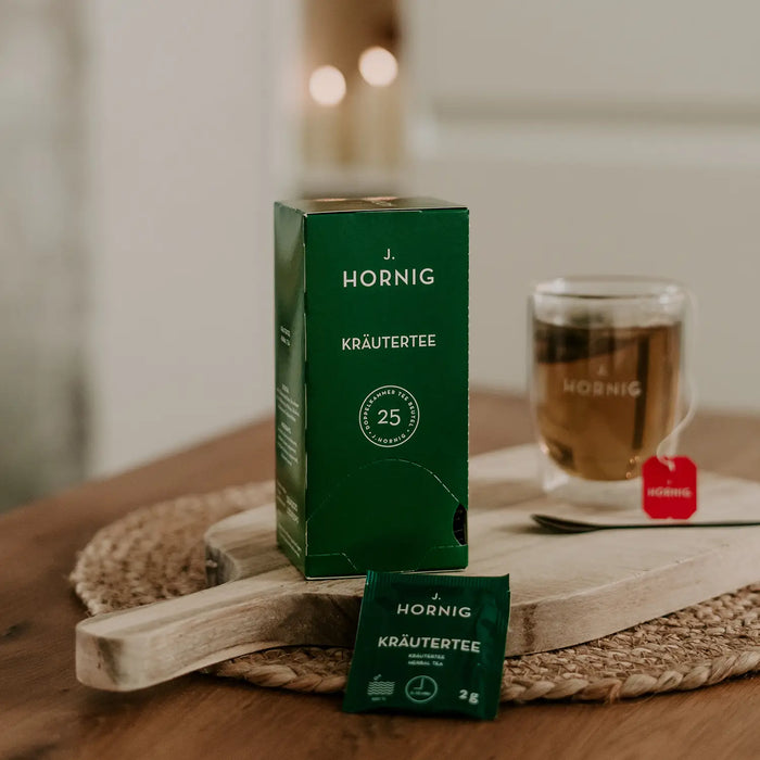 Eine Packung J.Hornig Doppelkammerbeutel Kräutertee auf einem Holztisch mit einer Tasse Tee.