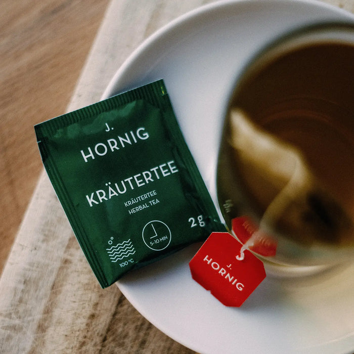 Eine Tasse Tee in einem J.Hornig Teeglas mit einer Einzelpackung Kräutertee.