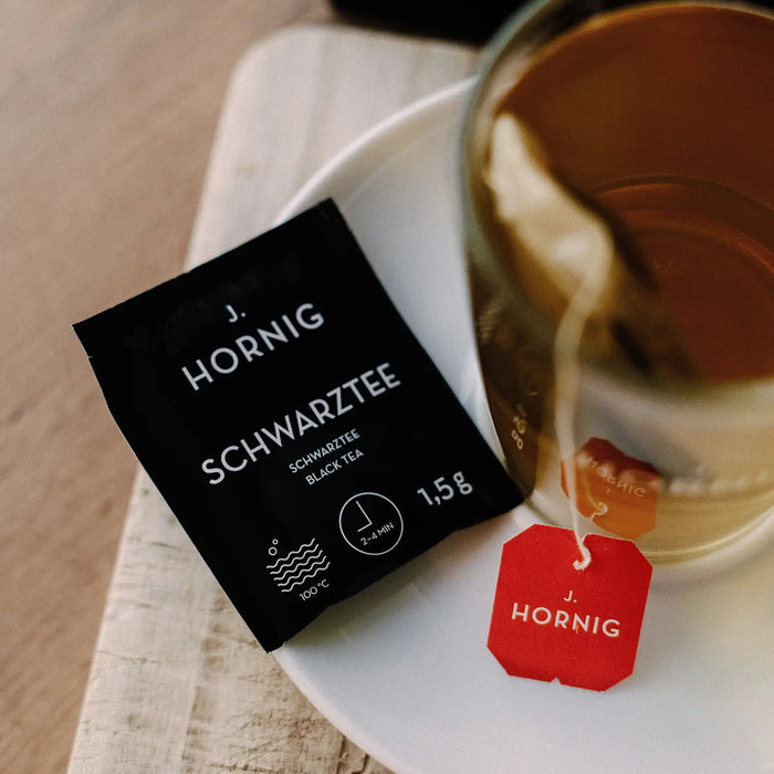Eine Tasse Tee in einem J.Hornig Teeglas mit einer Einzelpackung Schwarztee.