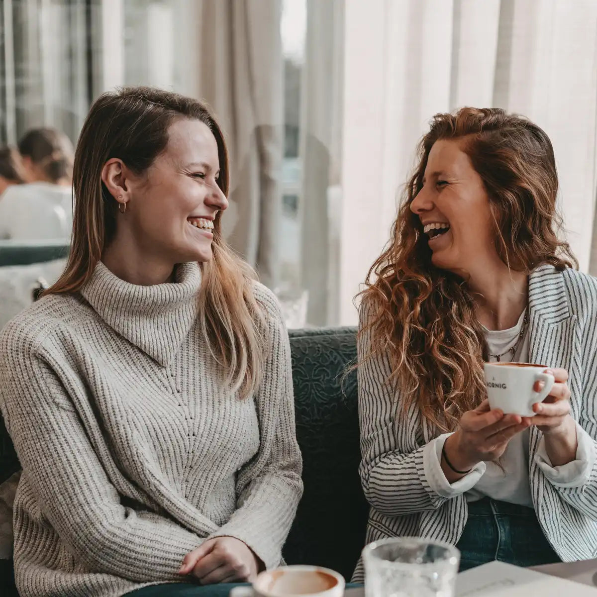 Zwei Frauen sitzen im Kaffeehaus, trinken Kaffee und unterhalten sich.