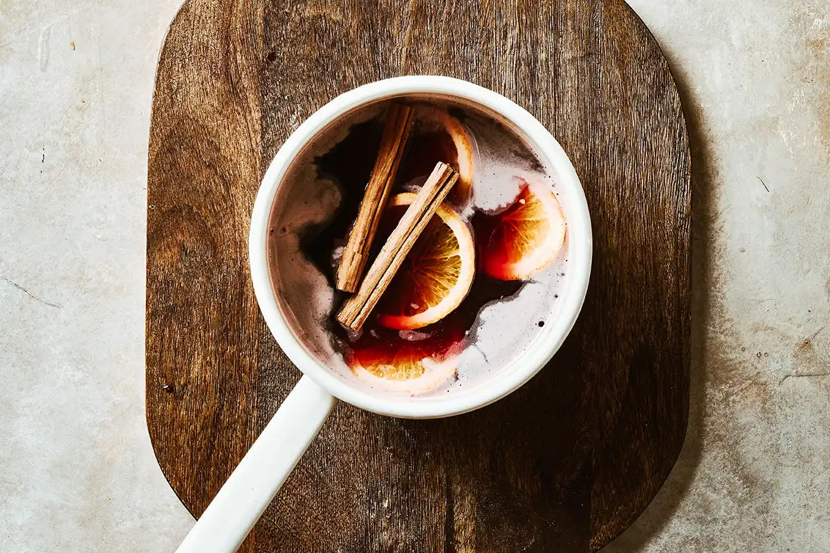 Ein Kochtopf mit Kaffee Glühwein, Zimtstangen und Orangenscheiben steht auf einem Holzbrett