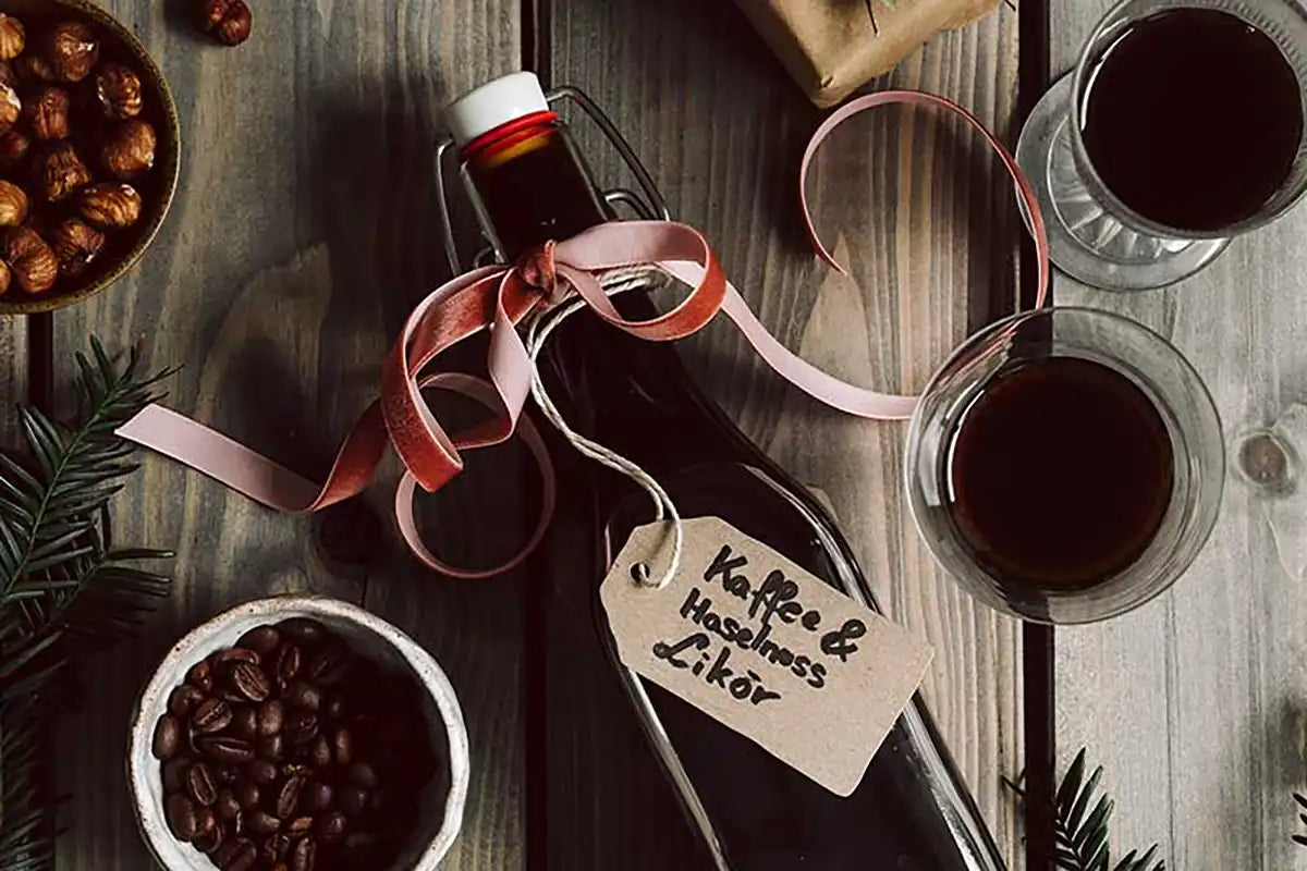 Eine Flasche Kaffee-Haselnuss-Likör liegt auf einem Tisch runderherum stehen Gläser mit Likör, Nüsse und Kaffeebohnen