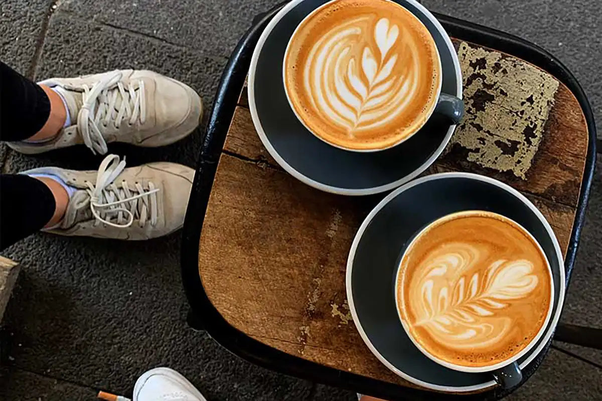 Zwei Tassen Cappuccino mit Latte Art stehen auf einem Holzbrett 