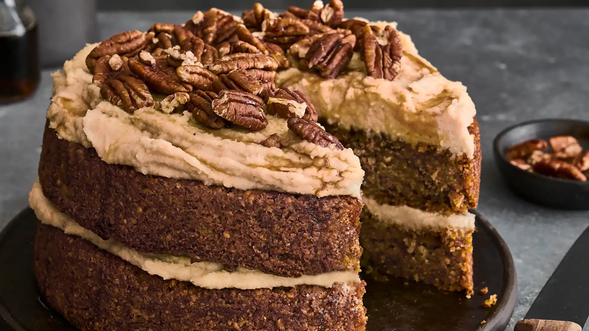 Vegane Kaffee-Karotten-Torte mit Pekannüssen garniert auf grau marmoriertem Untergrund