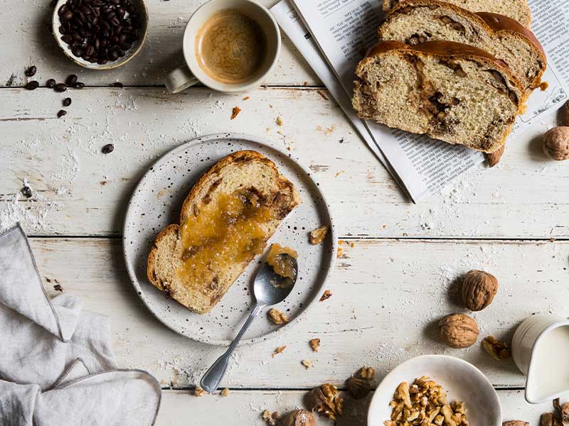 Ein veganes Walnuss-Kaffee-Osterbrot mit Marmeladen auf einem weißen Tisch.