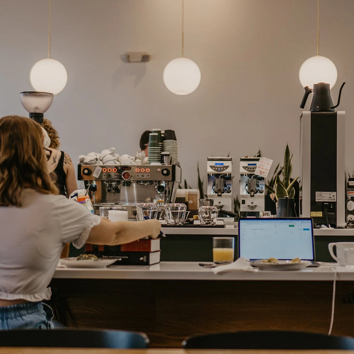 Eine Person sitzt an einer Theke in einem Coffeeshop mit einer Siebträgermaschine im Hintergrund