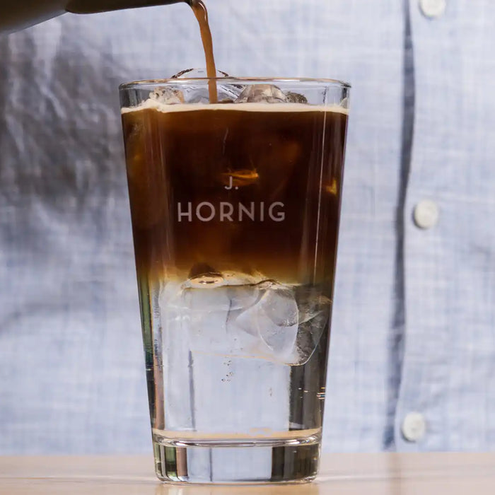 Ein Mann schüttet mit einer Hand Kaffee in ein Glas mit Eiswürfeln und Tonic