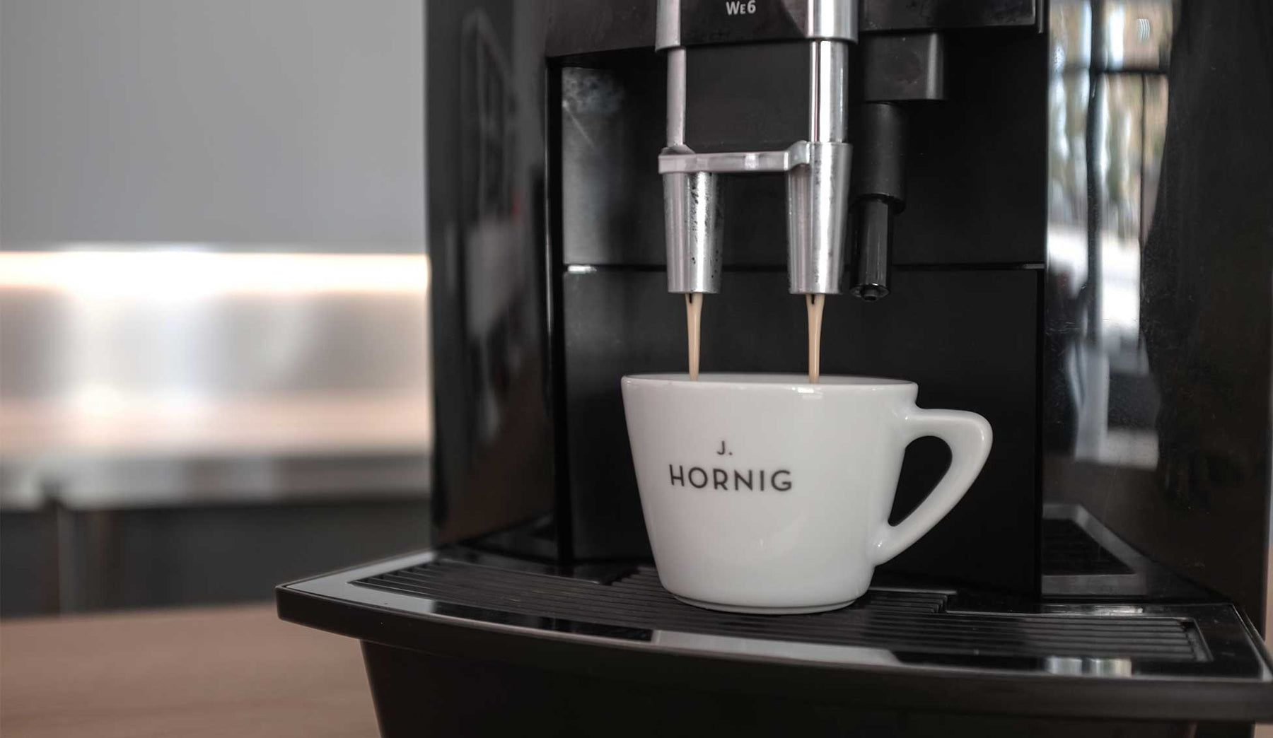Kaffee rinnt von einem Kaffeevollautomaten in eine weiße J. Hornig Tasse 