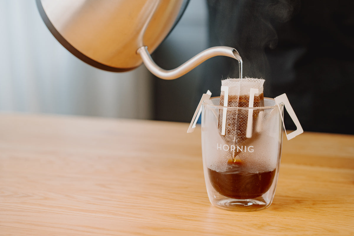 Eine Tasse mit dem Dripbag steht auf einem Tisch. Durch den Dripbag fließt der Filterkaffee.