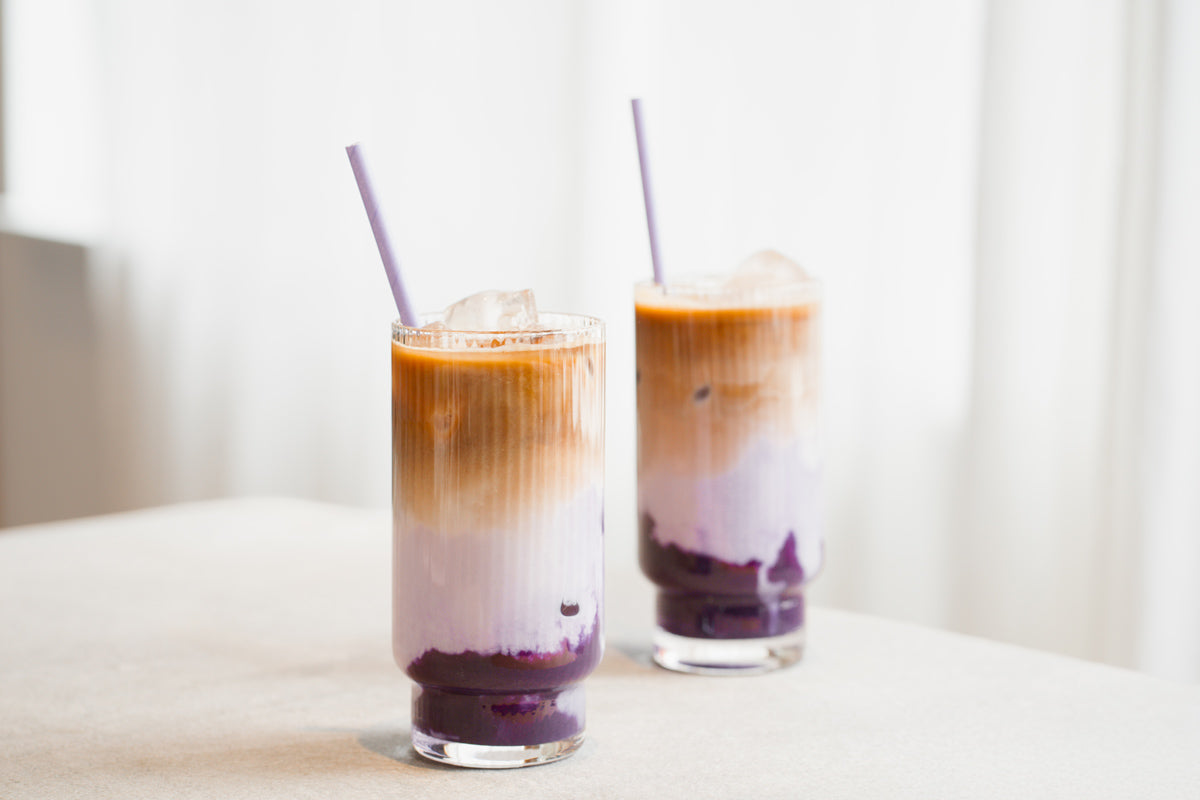 Zwei Ube Latte stehen auf einem Tisch mit hellem Hintergrund. 