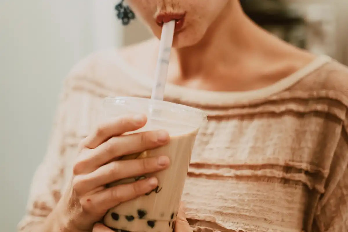 Frau trinkt durch einen Strohhalm Boba-Coffee aus einem To-Go-Becher