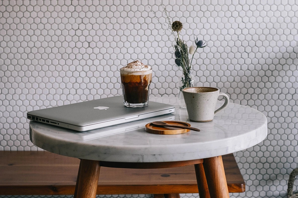 Ein Marmortisch mit einem Laptop, einem Kaffee im Glas und einer Tasse.