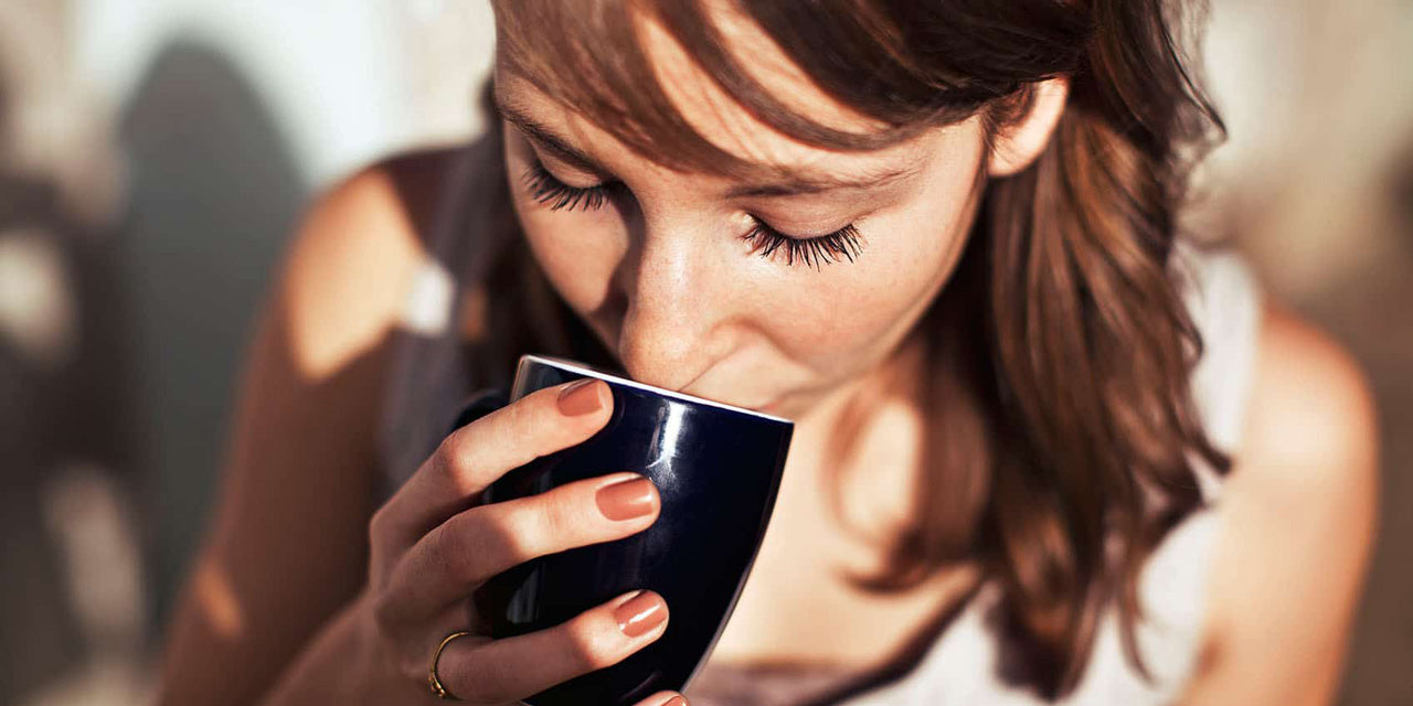 Frau trinkt Kaffee aus einer schwarzen Tasse.