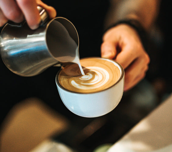 Eine Person kreiert den Milchschaum bei einem Cappuccino.