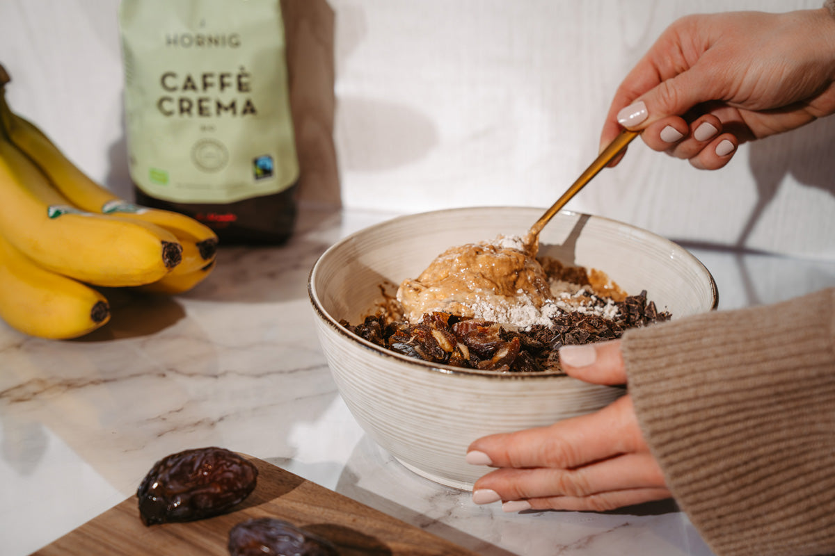 Der Teig für das Bananenbrot wird in einer Schüssel gemischt. Im Hintergrund ist Kaffee, Bananen und Datteln zu sehen.