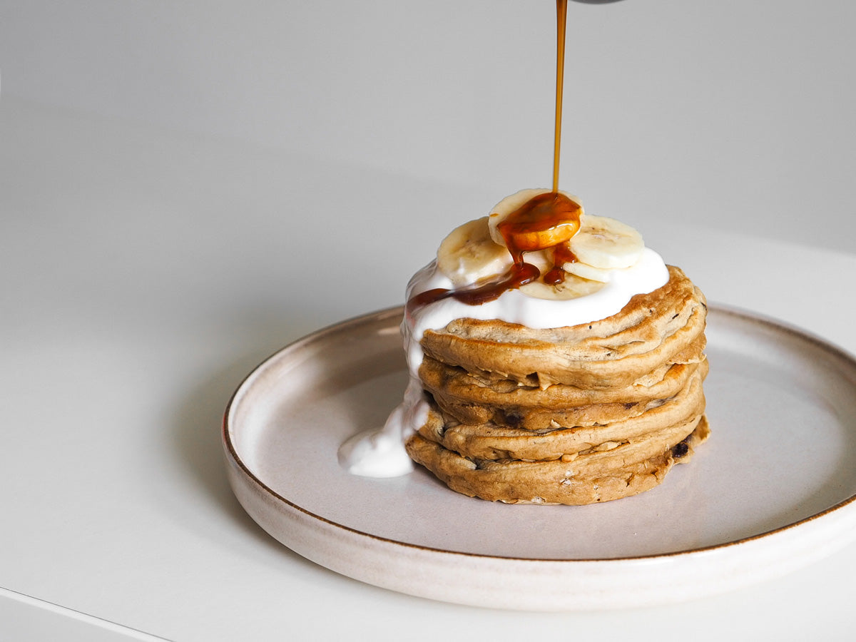 Coffee Chocolate Chip Pancakes mit Kokosjoghurt und Bananentopping die mit Sirup übergossen werden 