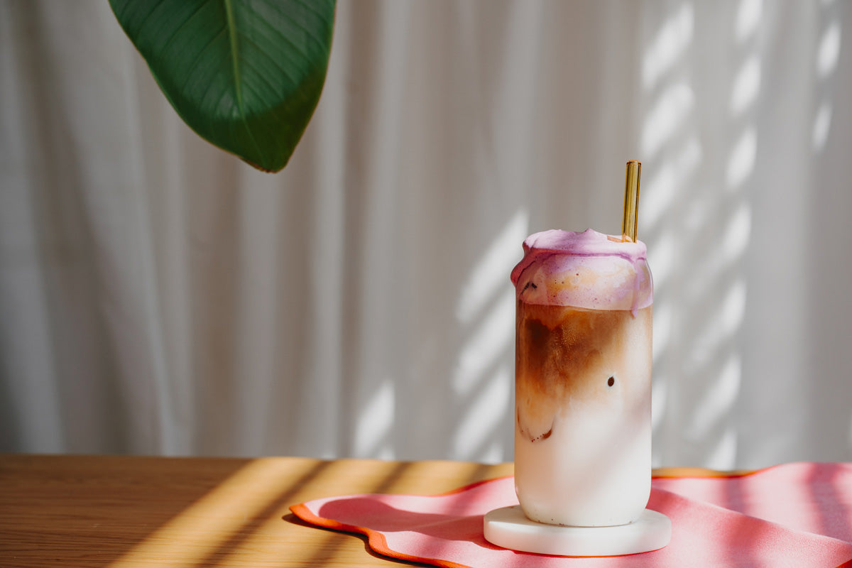 Ein Dirty Ube Latte steht auf dem Tisch, darin befindet sich ein gelber Strohhalm. 