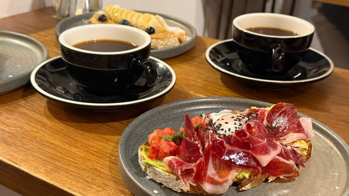 Gedeckter Tisch mit mehreren Frühstücksgerichten, darunter Avocado-Prosciutto-Toast, dazu Batch Brew/Filterkaffee.