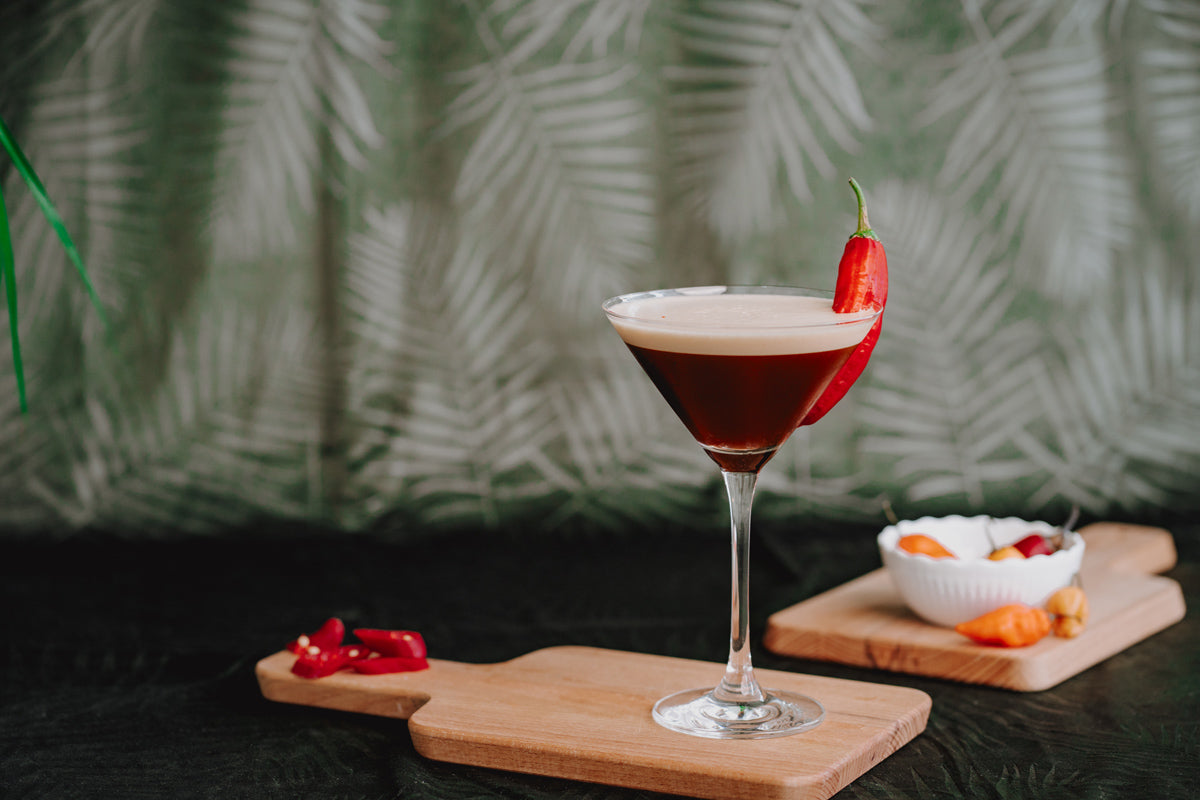 Swizy Espresso Martini garniert mit einer Chili auf einem Holzbrett.