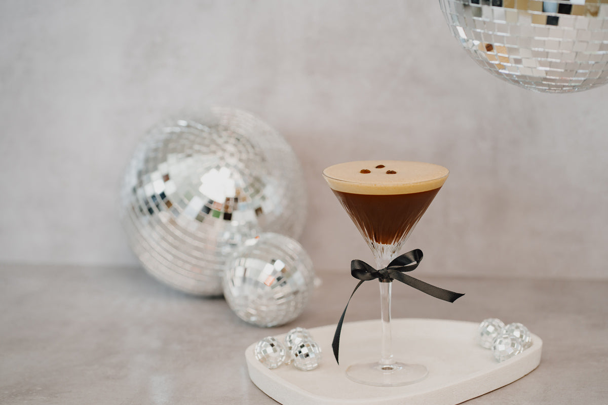 Entcoff No-tini in einem Martiniglas dekoriert mit einer Schleife mit Discokugeln im Hintergrund.