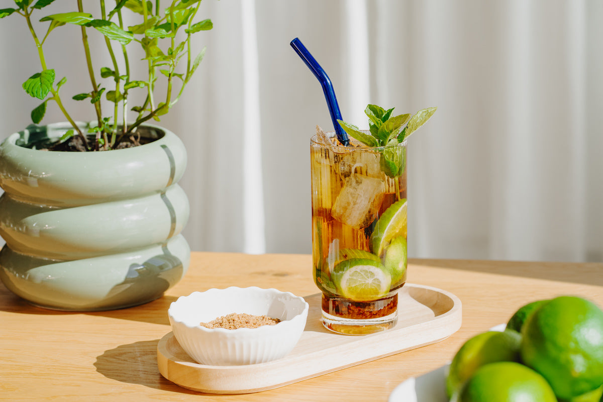 Der Cold Brew Mojito steht auf einem Tablett auf einem Tisch, im Hintergrund sind Minze und Limetten zu sehen.