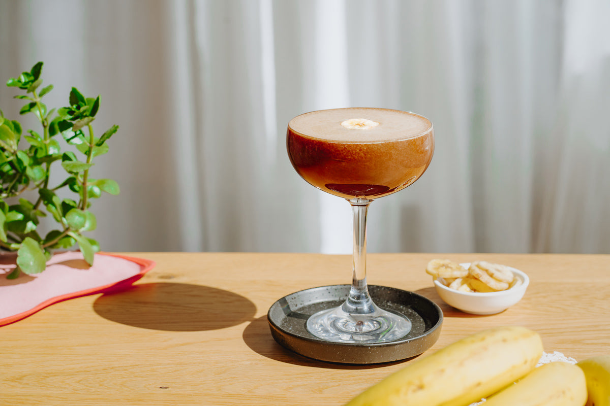 Der Drink steht auf dem Tisch, im Hintergrund sind Bananen und eine Pflanze zu sehen.