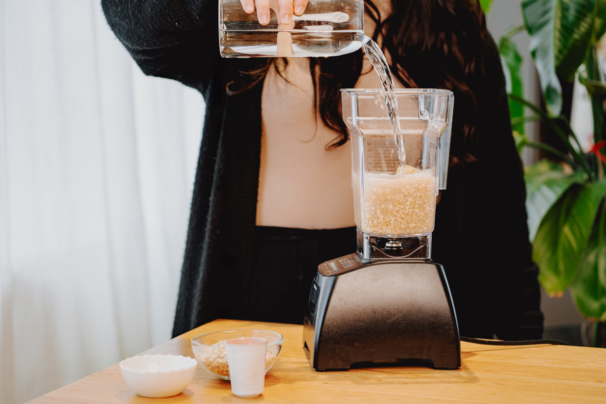 In einen Mixer, der auf einem Tisch steht, werden Haferflocken und Wasser geschüttet.