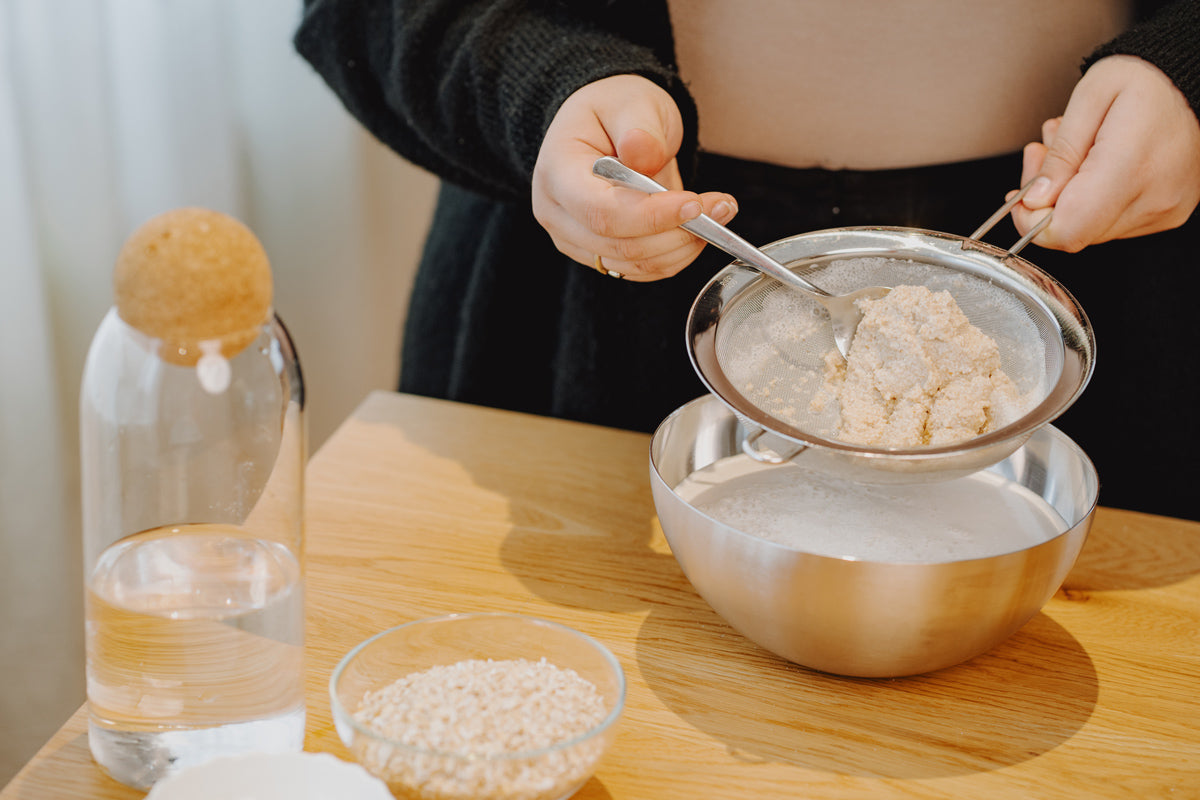 Die gemixten Haferflocken werden durch einen Sieb in eine Schüssel abgeseiht. In dem Sieb bleiben Haferreste hängen.