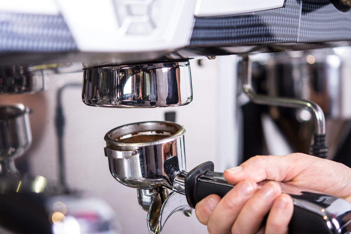 Ein Siebträger, gefüllt mit gemahlenem Kaffee, wird in die Brühgruppe eingespannt.